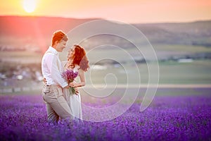 A loving couple standing in a lavender field and hugging. Beautiful bride dressed in luxurious wedding dress. Bride and