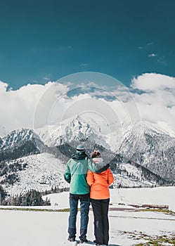 Milujúci pár stojaci a pri pohľade na krásne zasnežené vrcholky hôr. Vertikálny panoramatický pohľad. Pohľad zozadu