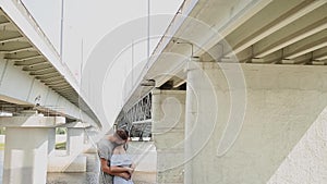 A loving couple are standing under a bridge hugging and kissing.