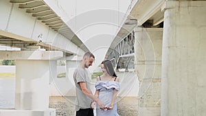 A loving couple are standing under a bridge hugging and kissing.