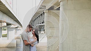 A loving couple are standing under a bridge hugging and kissing.