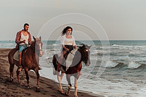 A loving couple in summer clothes riding a horse on a sandy beach at sunset. Sea and sunset in the background. Selective