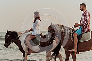 A loving couple in summer clothes riding a horse on a sandy beach at sunset. Sea and sunset in the background. Selective