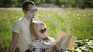 Loving couple in sunglasses at sunset read book on field with dandelions