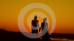 Loving couple at sunset - young man and beautiful girl stands at summer meadow and looking to sun, silhouette