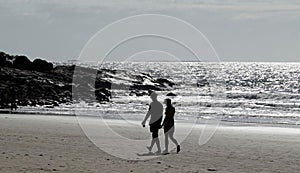 Loving couple walking hand in hand on a sandy beach towards the beautiful expanse of the ocean