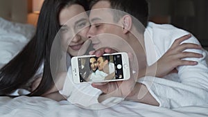 Loving couple in white coats on bed happily do selfie on a smartphone stock footage video