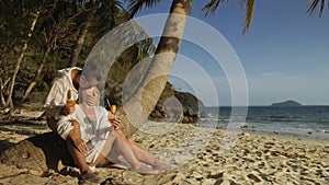 Loving couple in white dress and sunglasses, near palm tree, relax and drinking cocktail. Concept sea beach tropical