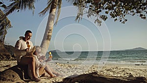 Loving couple in white dress and sunglasses, near palm tree, relax and drinking cocktail. Concept sea beach tropical