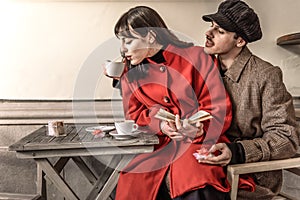Loving couple who are reading a book in the bar. Two gifts with red bow are placed on the table. The couple is drinking cappuccino