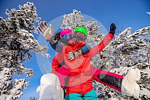 Loving couple woman and man having fun and fooling around in winter forest. Skier and snowboarder on background of blue