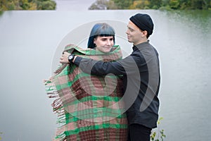 Loving couple wrapped in plaid sitting on mountain outdoors on sunset. River view. Man and woman traveling together.