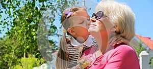 Loving cute granddaughter hugging and kissing her grandmother. Happy family.  Having good times with grandparent outdoors