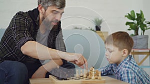 Loving dad is playing chess with his little child, teaching him rules and talking to him. Raising children, intellectual
