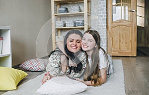 loving daughter hugs her happy mom lying on the floor in the house