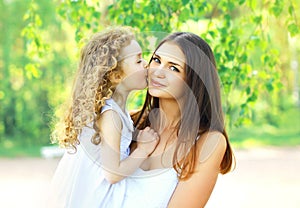 Loving daughter kissing mother, happy young mom and child in warm sunny summer day on the nature