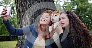 Loving dog owners girls taking selfie with pet in park using smartphone camera