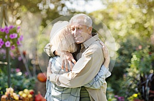 Loving elderly couple hugging each other during walk in their own garden in countyside, enjoying their vacation