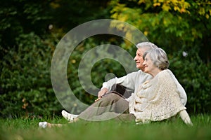 Portrait of elderly couple sitting on green grass in the summer park