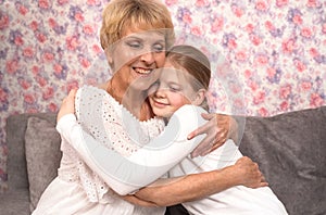 A loving elderly grandmother hugs and kisses her teenage granddaughter.