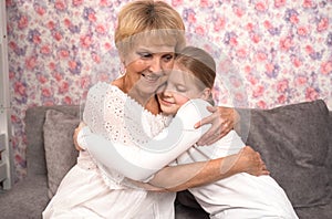 A loving elderly grandmother hugs and kisses her teenage granddaughter.