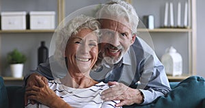 Loving elderly husband embracing sitting on couch smiling hoary woman.