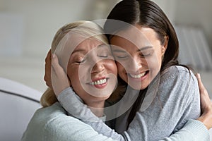 Loving elderly mother and adult daughter hug at home