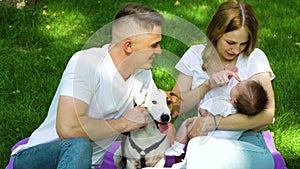 Loving family with baby and dog sitting on green lawn in park