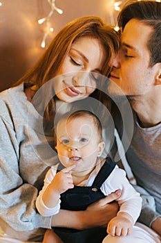 Loving family idyll, a daughter in the arms of her parents looks at the camera