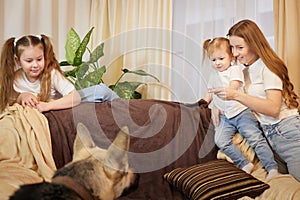 Loving family with mother, daughter sisters and big dog in living room. Woman mom, small child girl, female teenager who