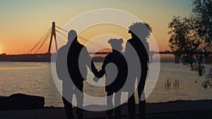 Loving family silhouette walking to river shore together at beautiful sunset.