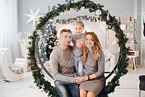 Loving family snuggling on Christmas swing. Christmas tree.