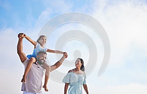 Loving father carrying his daughter on his shoulders while walking along the beach with his wife against a cloudy sky