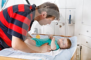 Loving father changing diaper of his healthy newborn baby daughter. Little child, girl on changing table in bathroom