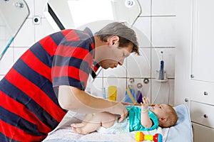 Loving father changing diaper of his newborn baby daughter. Little child, girl on changing table in bathroom with rattle