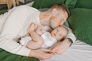 Loving father lies on the bed with his baby son, hugs him and kisses him