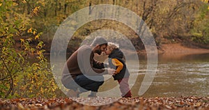 Loving father and little son are communicating at nature, on shore of lake at autumn day, man and boy are snuggling by