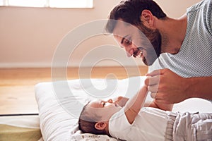 Loving Father Lying With Newborn Baby On Bed At Home In Loft Apartment