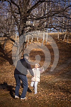 Loving father playing with little daughter both having fun and smiling having walk in forest with dry fallen leaves on