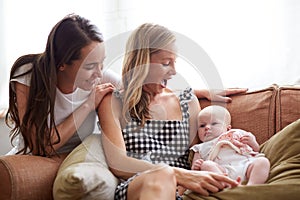 Loving Female Same Sex Couple Cuddling Baby Daughter On Sofa At Home Together