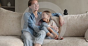 Loving foster mother and preteen adopted daughter cuddle on sofa