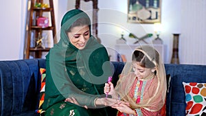 A loving girl child spending quality time with her caring mother while decorating her hand with Henna