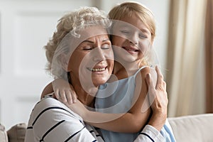 Loving grandmother cuddle snuggle to small granddaughter enjoy moment closeup