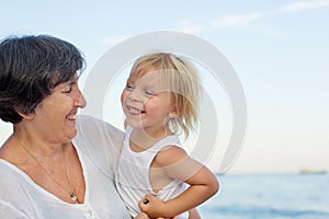 Loving grandmother and grandson, blond toddler boy, hugging at the beach, enjoying time