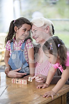 Loving grandmother teaching calculation to granddaughters at table in house