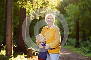 Loving grandson tenderly embracing his joyful elderly grandmother during walking at summer park