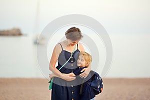 Loving grandson tenderly embracing his joyful mature grandmother while walking on sea shore. Two generations of family