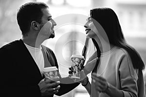 Loving happy couple looking to each other on the background of window and holding cups in their hands. Black and white