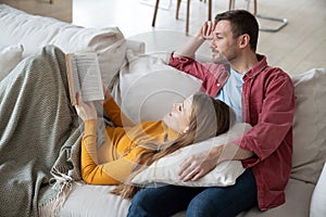 Loving happy couple spending weekend together at home, reading and discussing interesting novel book