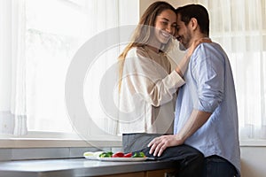 Loving happy newlyweds cuddle cooking in kitchen at home